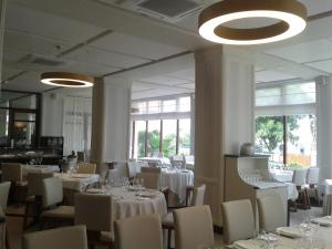 un restaurante con mesas y sillas blancas y ventanas en Las Rocas Playa Hotel, en Castro Urdiales