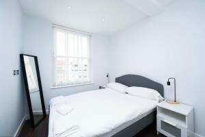 a white bedroom with a bed and a mirror at Stylish 3BR Flat in the Heart of Soho London in London