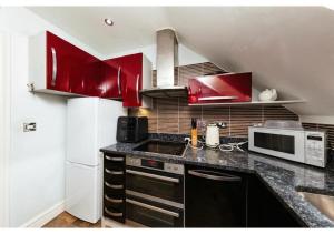 a kitchen with red cabinets and a white refrigerator at Chic Croydon 2BR Flat - Free Parking in Purley