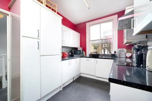 a kitchen with white cabinets and a red wall at Chic and comfortable London 2BR home in London