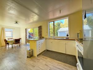 cocina con armarios blancos, mesa y ventanas en 45 Scarborough Terrace, en Hanmer Springs
