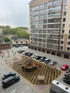 um parque de estacionamento com carros estacionados em frente a um grande edifício em Апартаменти в центрі на Проскурівського Підпілля em Khmelʼnytsʼkyy