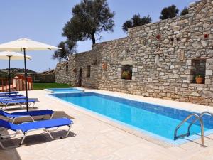 Una piscina con sillas y una sombrilla junto a un muro de piedra. en Leonidas Comfortable holiday residence, en Pitsidia