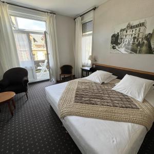 バニョール・ドゥ・ロルヌにあるBrit Hotel Confort Bagnoles Normandieのベッドと大きな窓が備わるホテルルームです。