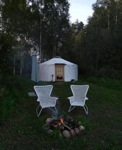 duas cadeiras e uma lareira num quintal com uma tenda em Glamping Yurt Purvs at Kleja Quiet Camping em Eikaži