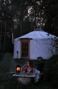 una donna seduta in un letto di fronte a una tenda di Glamping Yurt Purvs at Kleja Quiet Camping a Eikaži