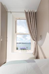 een witte slaapkamer met een raam met paarse bloemen bij Unit 2 Island View Apartments With Stunning Harbour View in Cobh