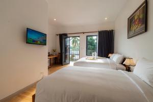 a bedroom with two beds and a tv on the wall at Aurora House in Phú Quốc