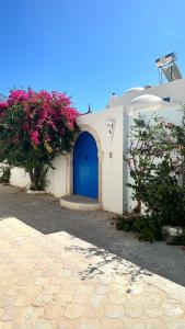 een wit gebouw met een blauwe deur en roze bloemen bij Séjour de Sarber in Taguermess