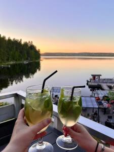 two people holding drinks with a view of a river at Boutique-hotelli Vellamo - Lehmonkärki Resort in Asikkala
