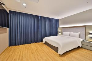 a bedroom with a large white bed and blue curtains at Gimhae City Hotel in Gimhae