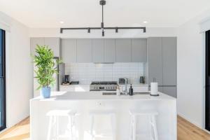 una cocina blanca con encimera blanca y taburetes en Coastal Elegance, Torquay, en Torquay