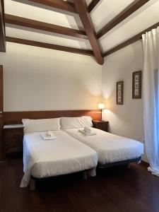 1 dormitorio con 2 camas, sábanas blancas y techos de madera. en Casa Boado, en Boimorto