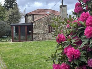 una casa de piedra con flores rosas delante de ella en Casa Boado, en Boimorto