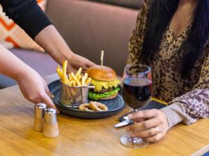 a hamburger and french fries on a table with a glass of wine at ibis London City - Shoreditch in London