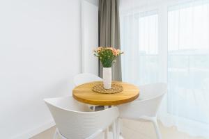 uma mesa com cadeiras brancas e um vaso com flores em Aquamarina Prima Deluxe Studios With Sea View by Renters em Międzyzdroje
