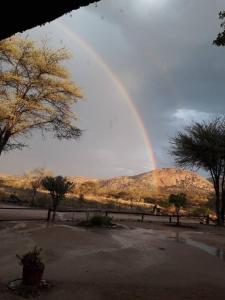 un arco iris en el cielo sobre un campo con árboles en Camp Mara, en Omaruru