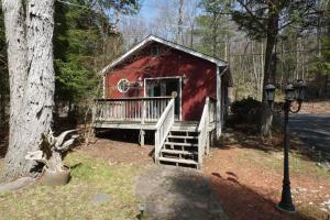 a red shed with a porch and stairs in a forest at Catskills Lakefront Escape with Hot Tub in Monticello