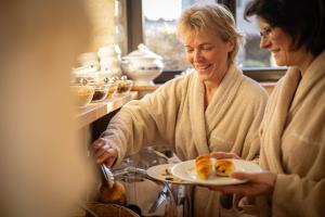 dos mujeres mayores sentadas juntas sosteniendo un plato de comida en Thermae Boetfort Hotel en Steenokkerzeel