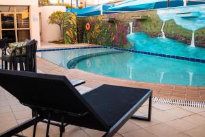 a swimming pool with two chairs and a bench next to it at Hotel Golden Park Uberlandia in Uberlândia