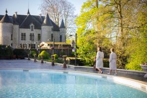 dos mujeres caminando por una piscina frente a un castillo en Thermae Boetfort Hotel, en Steenokkerzeel