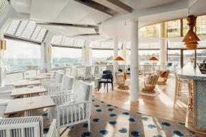 un restaurant avec des chaises blanches, des tables et des fenêtres dans l'établissement Emeria Dinard Thalasso Spa - Avril 2024 Réouverture après rénovation, à Dinard
