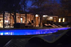 a woman sitting on a couch next to a swimming pool at night at Hotel La Aldea in San Pedro de Atacama