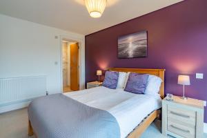 a bedroom with a large bed with a purple wall at Muntjac Lodge in Somerford Keynes