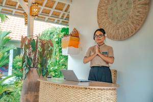 Tulus Hati Ubud Retreat في أوبود: امرأة تقف أمام طاولة مع جهاز كمبيوتر محمول