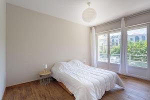 a white bedroom with a bed and a large window at Appartement d'exception proche des commerces avec piscine in Biarritz