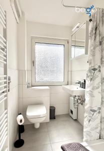 een badkamer met een toilet, een wastafel en een raam bij BEGE APARTMENTS Business Residence in Hagen