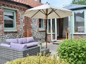 a patio with an umbrella and a purple couch at Gryngolet Cottage - with Artist Studio - Crabpot Cottages Sheringham in Aylmerton