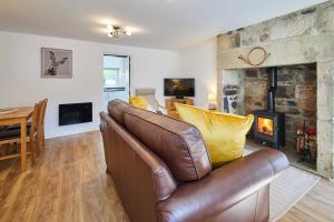 a living room with a leather couch and a fireplace at Host & Stay - Rose Cottage in Thropton