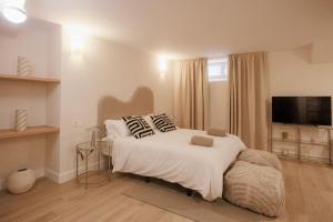 um quarto com uma cama branca com almofadas e uma televisão em Apartamentos Cervantes em Badajoz