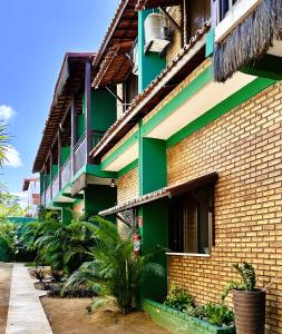a green building with palm trees in front of it at Suítes Green Village Flecheiras in Flecheiras