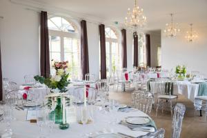 een eetkamer met witte tafels en stoelen en kroonluchters bij Domaine Les Jardins dArsene in Tinténiac