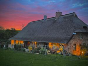 una casa con techo de paja y una puesta de sol en el fondo en idyllisch gelegenes Ferienhaus nähe Heiligenhafen, en Gremersdorf