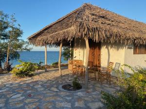 Namahamade Lodge Restaurante & Beach Bar في Mossuril: كوخ مع كراسي وطاولة أمام المحيط