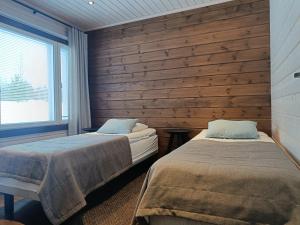 two beds in a room with a wooden wall at Rantatähti Villa in Syöte