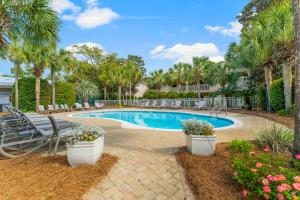 a swimming pool with benches and palm trees at Cassine Gardens by Panhandle Getaways in Santa Rosa Beach