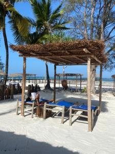 a person laying on the beach under a straw umbrella at Kiwengwa Bungalow Boutique Resort in Kiwengwa