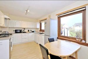 une cuisine avec des placards blancs, une table et une fenêtre dans l'établissement Sunny Cove Holiday Let, à Aberdeen