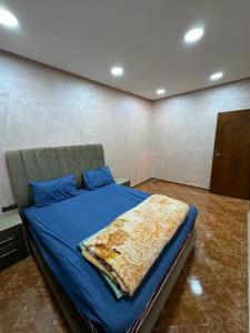 ein Schlafzimmer mit einem Bett mit einer blauen Decke darauf in der Unterkunft appartement spacieux in Deroua