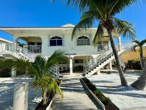 une maison blanche avec des palmiers devant elle dans l'établissement Easy Ocean Access 30' Dock - House - Private Club w/ Heated Pool and Sandy Beach, à Key Colony Beach