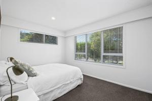 Un dormitorio blanco con una cama y dos ventanas. en Te Moenga Treasure - Acacia Bay, en Taupo