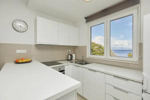 a white kitchen with a clock and a window at Apartments by the sea Sobra, Mljet - 22343 in Babino Polje