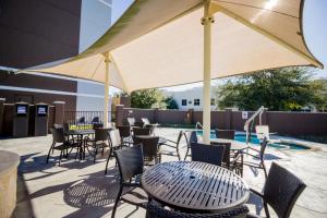 un patio con mesas, sillas y una sombrilla grande en Atwell Suites Austin Airport, an IHG Hotel en Austin