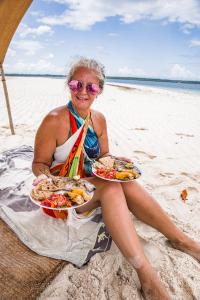 una mujer sentada en la playa con dos platos de comida en Afro Rooms & Tents in The Beach en Kilindoni