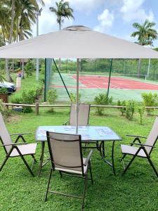 Grand-BourgにあるLa Kawanaise Blue Lagonのテニスコートのパラソルの下にテーブルと椅子