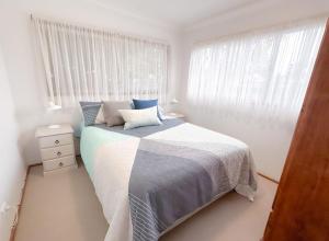 a white bedroom with a bed and a window at Collingwood Beach Cottage - Belle Escapes Jervis Bay in Vincentia